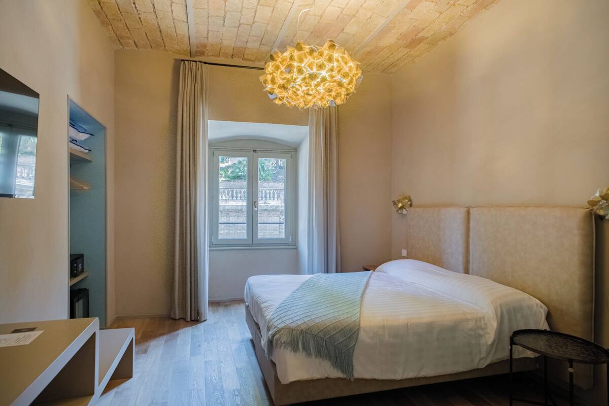 A bedroom with a bed, a desk, a chair, a ceiling light, and a window with curtains.