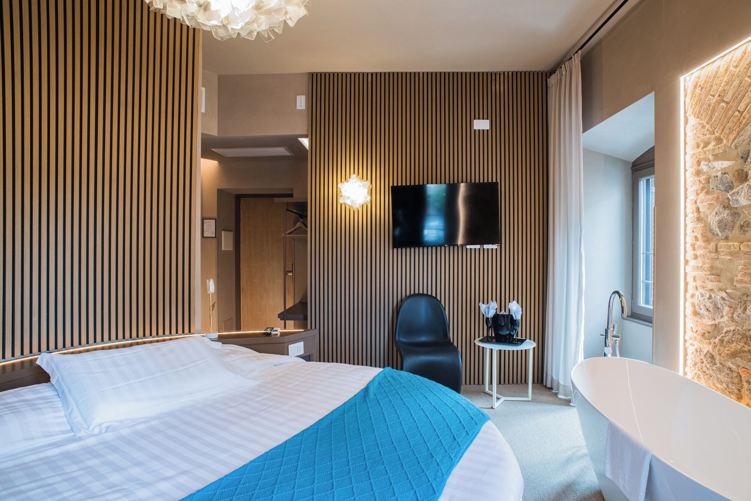 Ein modernes Hotelzimmer mit einem großen Bett, einem flachbildfernseher an der Wand, einem separaten Badezimmer mit einer Badewanne und einer Wand mit Steinverkleidung.