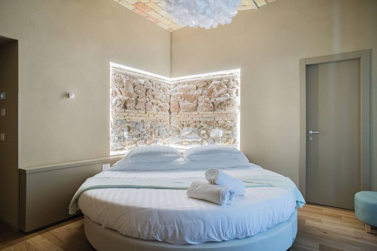 A modern bedroom with a round bed, a stone accent wall, and a wooden floor.