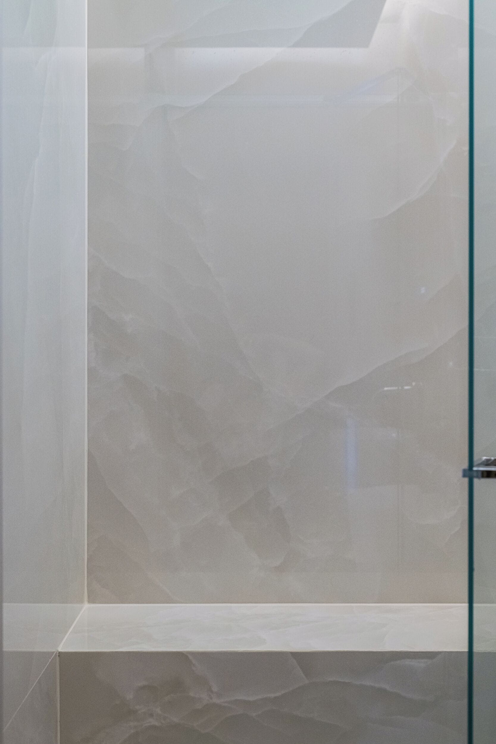 A bathroom with a marble wall and a glass shower enclosure.