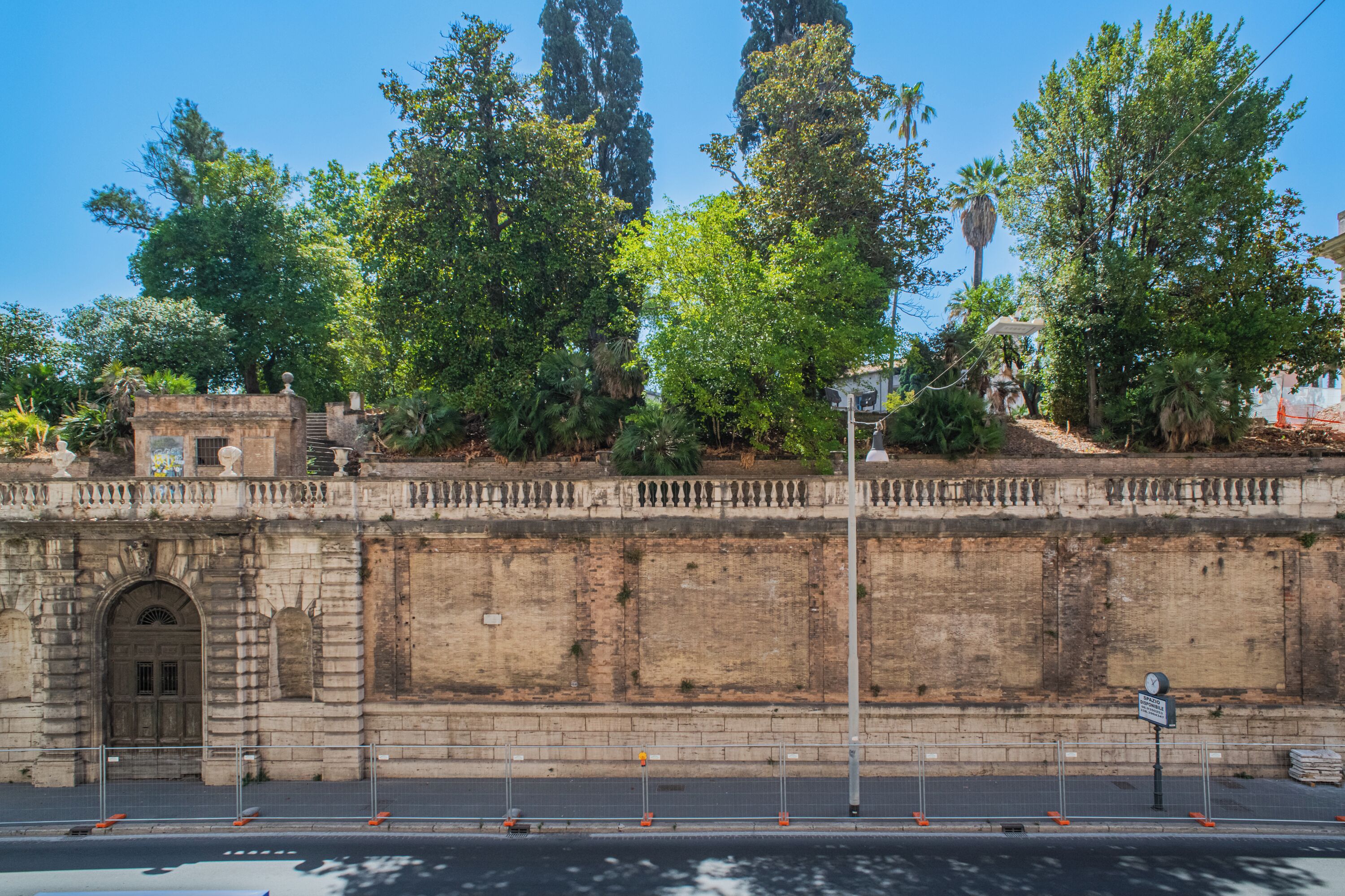 Een historische stenen muur met een poort, omringd door weelderig groen en bomen.