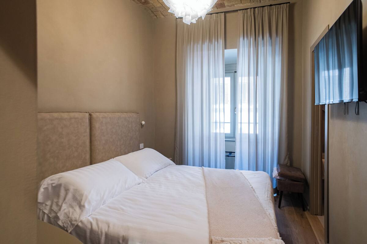 A bedroom with a bed, a chair, and a window with curtains.