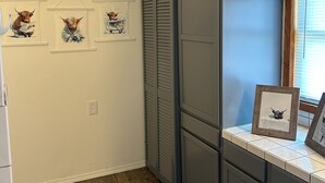Een keuken met houten vloeren, een raam met zonwering en drie ingelijste foto’s aan de muur.