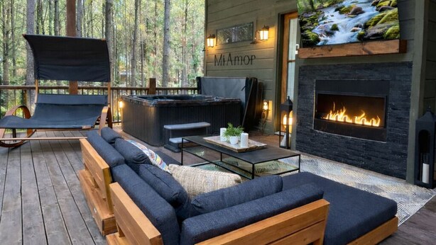 A cozy outdoor living area with a large sofa, a hot tub, and a fireplace.