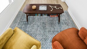 A spacious room with a high ceiling, a ceiling fan, a dark-colored sofa, a wooden coffee table, two chairs, and a patterned rug. - Best Value 2BR Midtown Stay - Clean + Central (Omaha)
