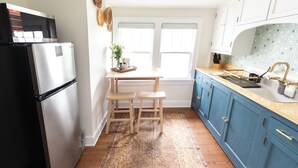 A kitchen with a refrigerator, a wooden table with two chairs, a window, and blue cabinets. - Best Value 2BR Midtown Stay - Clean + Central (Omaha)