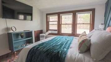 A bedroom with a bed, a TV mounted on the wall, a window, and a desk with a chair.