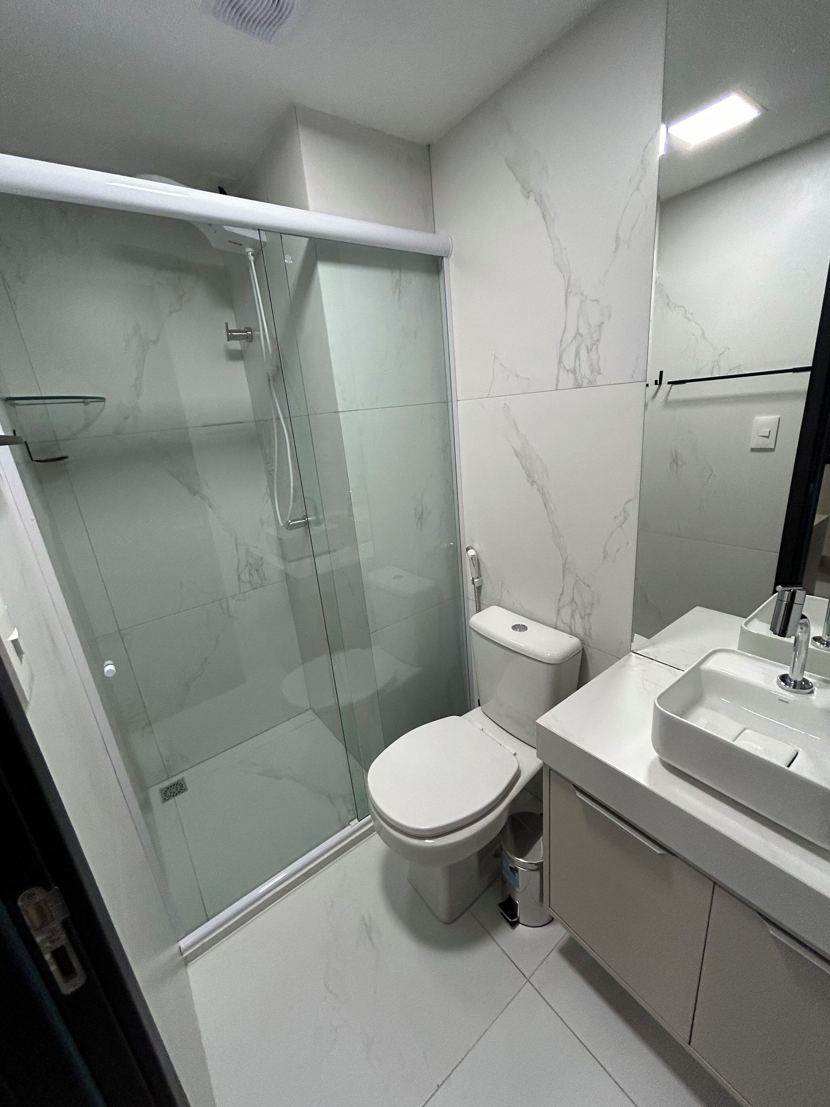 Un baño moderno con ducha de vidrio, inodoro y lavabo con espejo.
