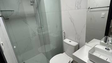 Un baño moderno con ducha de vidrio, inodoro y lavabo con espejo.