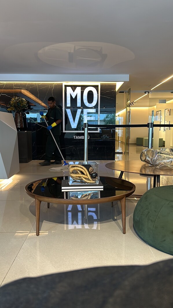 A modern interior with a 'MOVE' sign, a glass table with a sculpture, and a green ottoman. - Melhores Flats - Perfeição perto do mar (João Pessoa)