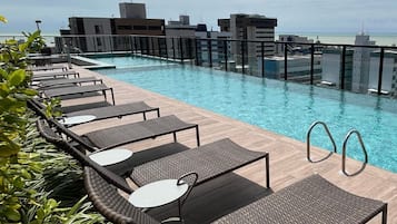 Piscina en la azotea con sillones de descanso y vista al horizonte de la ciudad.