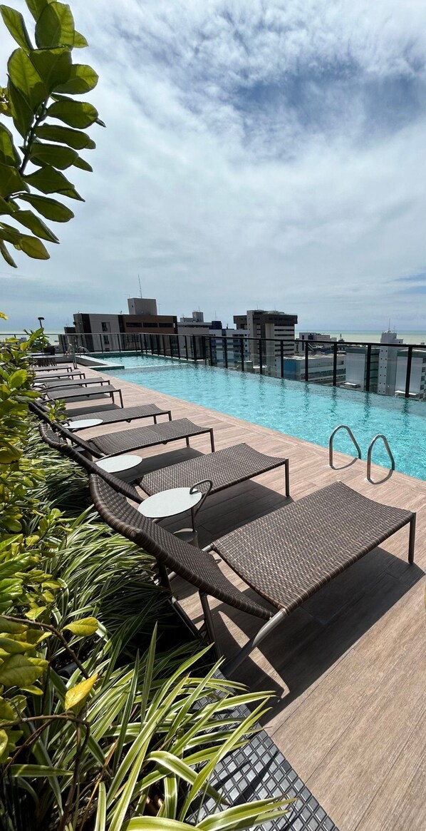 A rooftop pool with lounge chairs and a view of the city skyline. - Melhores Flats - Perfeição perto do mar (João Pessoa)