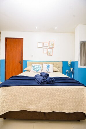 A bedroom with a bed, a wooden door, a small table with a potted plant, and framed pictures on the wall. - Suli Pousada (Florianópolis)