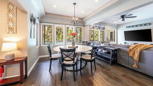 A spacious living room with a dining area, large windows, a ceiling fan, and a flat-screen TV. - La Jolla Beach House. 2 Minute Walk to the Beach! (San Diego)