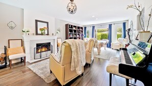 A spacious living room with a fireplace, a piano, and a large window with curtains. - La Jolla Beach House. 2 Minute Walk to the Beach! (San Diego)