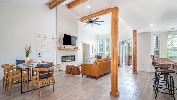A spacious living area with a wooden ceiling, a sofa, a dining table with chairs, and a TV mounted on the wall.