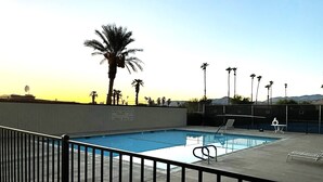 A swimming pool with a metal fence, a lifeguard chair, and palm trees in the background.