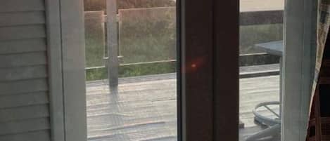 A view through a sliding glass door of a sunset over a body of water, with a deck and outdoor furniture visible.