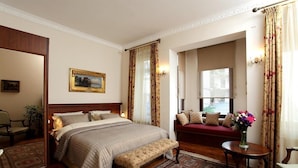 A hotel room with a large bed, a bench, a sofa, a small table, and a window with curtains. - Dila Suites (Istanbul)