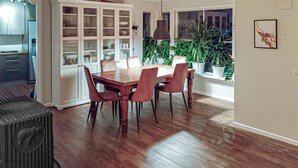 A dining area with a wooden table and chairs, a kitchen with white cabinets, and a view of the outdoors through a large window. - 3 bedroom stunning home in Avaldsnes (Avaldsnes)