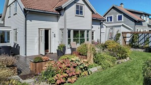 A two-story house with a red-tiled roof, a front porch with outdoor seating, and a well-maintained garden. - 3 bedroom stunning home in Avaldsnes (Avaldsnes)