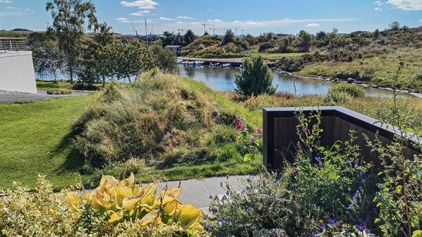A riverside view with a modern building, a dock, and boats. - 3 bedroom stunning home in Avaldsnes (Avaldsnes)