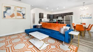 A modern living room with a blue sofa, orange rug, and a dining area with orange chairs. - Beautiful Home Walk to UF  Newly built (Gainesville)