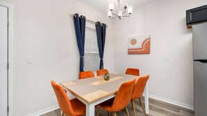 A dining area with a wooden table and orange chairs, a chandelier, and a window with curtains. - Beautiful Home - Walk to UF - Newly built (Gainesville)