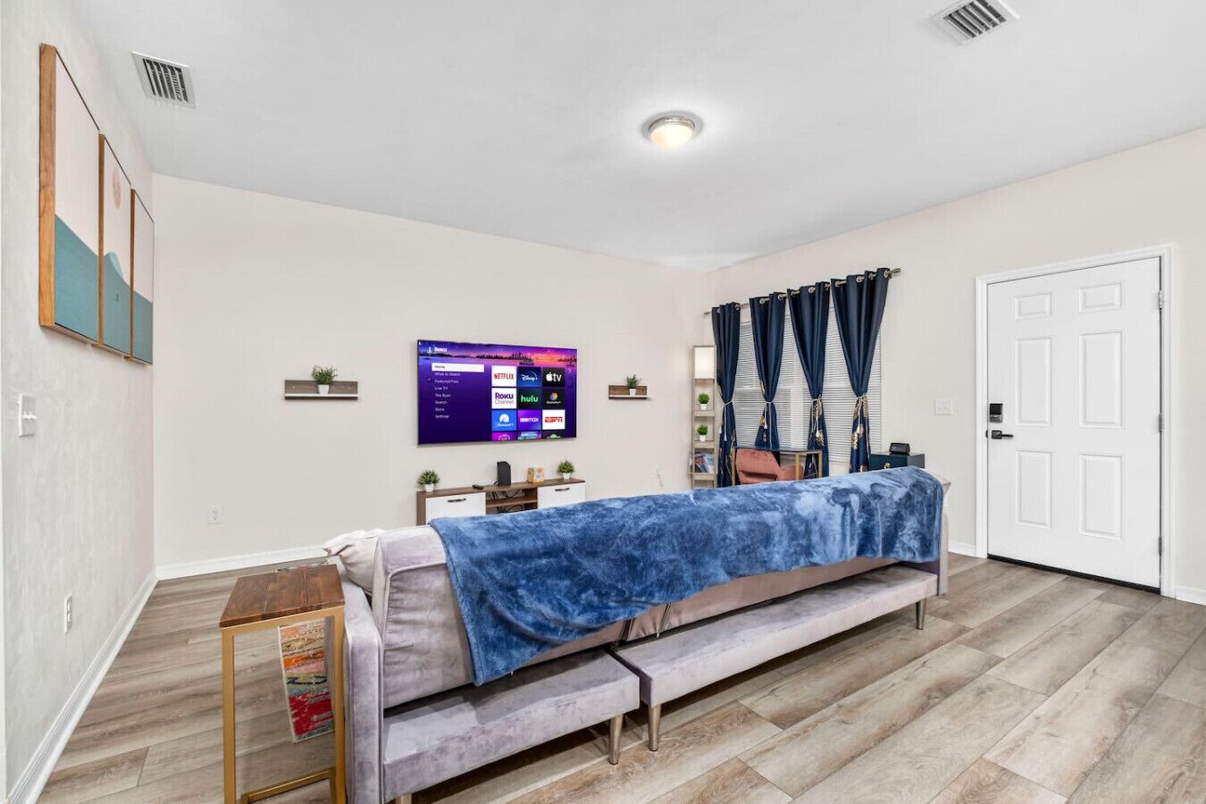 A bedroom with a bed, a flat-screen TV mounted on the wall, a door, and a window with curtains.