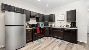 A modern kitchen with dark cabinets, stainless steel appliances, and a wooden floor. - Beautiful Home - Walk to UF - Newly built (Gainesville)