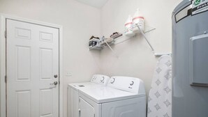 A laundry room with a front-loading washer and dryer, a shelf with cleaning supplies, and a door. - Beautiful Home - Walk to UF - Newly built (Gainesville)