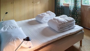 A neatly made bed with white linens, a bedside lamp, and a wooden wardrobe in the background.