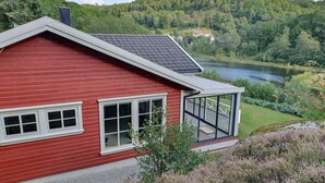 A red house with a large glass balcony overlooking a lake and forested hills.