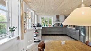Una cocina moderna con techo de madera, ventanas amplias y un comedor con mesa y sillas.