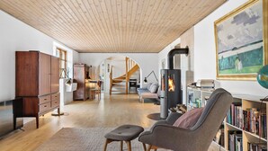 Un salón amplio con techo alto, chimenea, escalera y una estantería llena de libros.