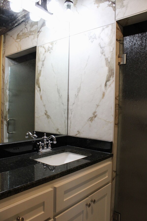 A bathroom with a marble wall, a sink with a faucet, and a mirror. - 7Js Waco Western Club - Privacy, View, Pool & Hot Tub (Riesel)