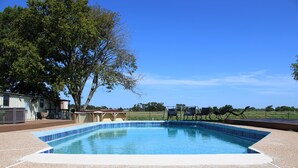 Una piscina sotto un cielo azzurro, circondata da un patio con sedie e una zona relax coperta.