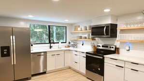 A modern kitchen with stainless steel appliances, white cabinetry, and a large window providing a view of greenery.
