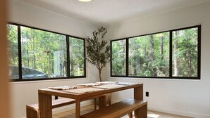 A room with a wooden table and benches, large windows with a forest view, and a potted plant.