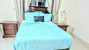 A neatly made bed with a quilted blue bedspread and a brown skirted bed base. - Don Juan Bungalow (Ocho Rios)