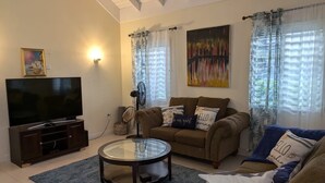 A living room with a flat-screen TV, a glass coffee table, a brown sofa, and a blue rug. - Don Juan Bungalow (Ocho Rios)