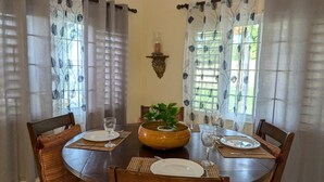 A dining room with a round table set for four, surrounded by chairs with striped cushions. A wooden bowl with a plant is placed in the center. - Don Juan Bungalow (Ocho Rios)