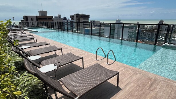 A rooftop pool area with lounge chairs and a view of the city skyline. - Melhores Flats (João Pessoa)