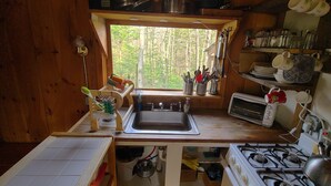 Cocina compacta con vista al exterior, un lavamanos, estufa y diversos utensilios y vajilla.