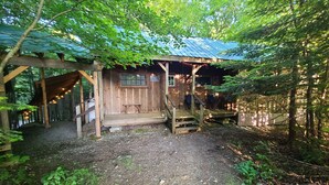 Una cabaña de madera rústica con porche, rodeada de un bosque denso.