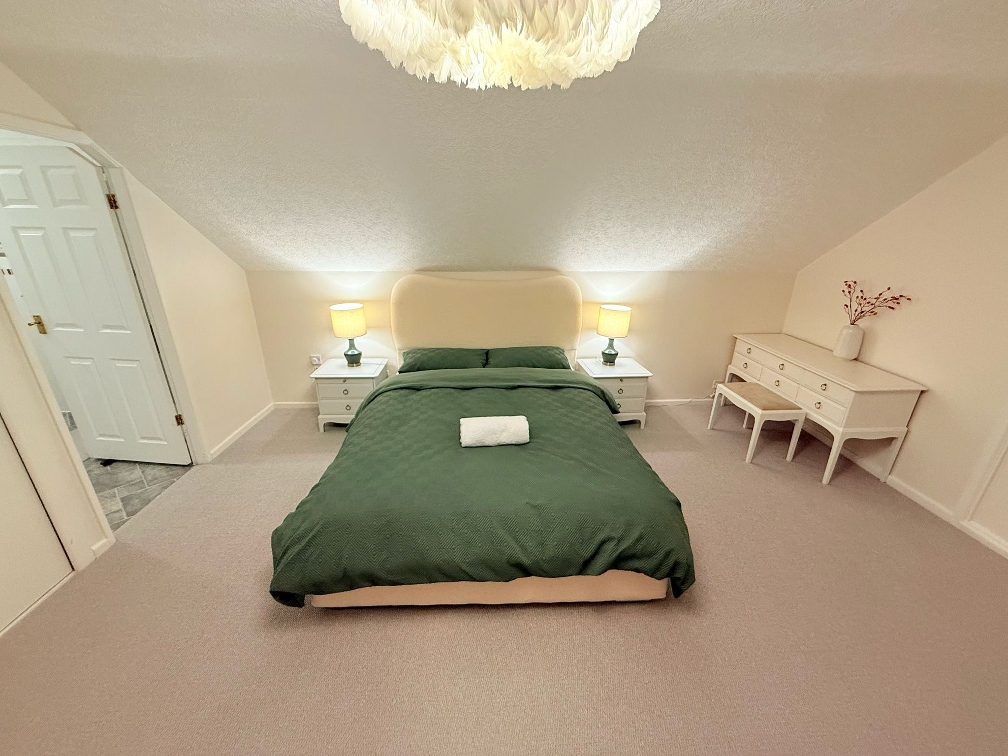 Ett sovrum med en stor säng, två sängbord med lampor, en byrå och en dörr.