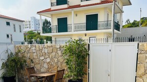 Un edificio de dos plantas con muro de piedra, entrada con puerta de rejas y un patio con mesa y sillas.