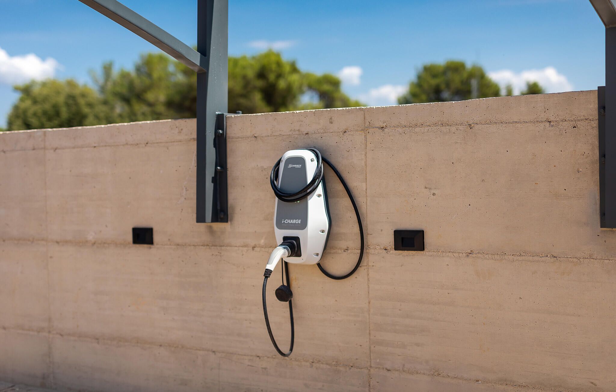 Une borne de recharge pour véhicules électriques i-CHARGE, fixée à un mur en béton.