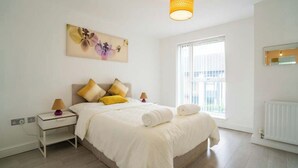 A bedroom with a bed, bedside lamps, a painting, a window, and a radiator.