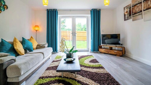A living room with a sofa, coffee table, and TV. There is a sliding glass door leading to a backyard.